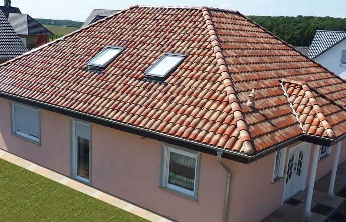Крыша частного дома с установлеными окнами-люками из черепицы, солнечная погода, зеленый ландшафт, уютное дачное строительство.