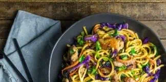 Запечённые лапша с овощами и курицей, азиатский стиль, в миске, на деревянном столе.