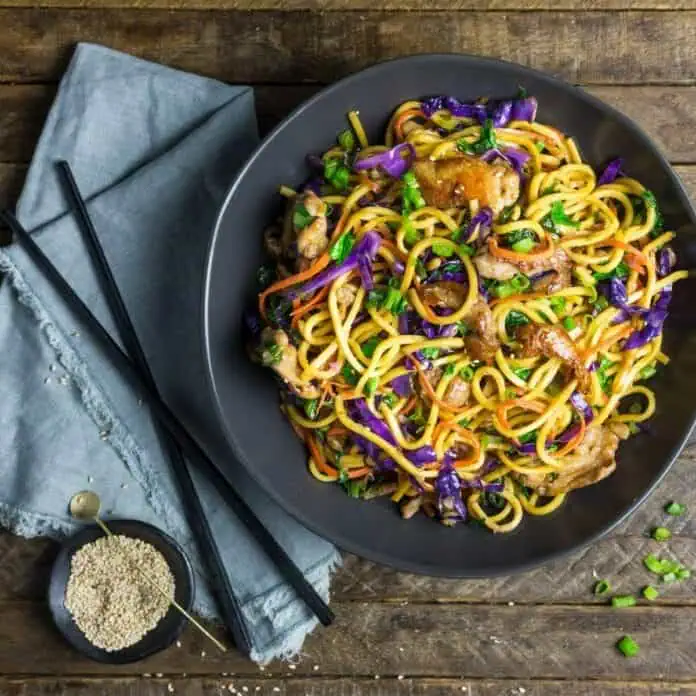 Запечённые лапша с овощами и курицей, азиатский стиль, в миске, на деревянном столе.