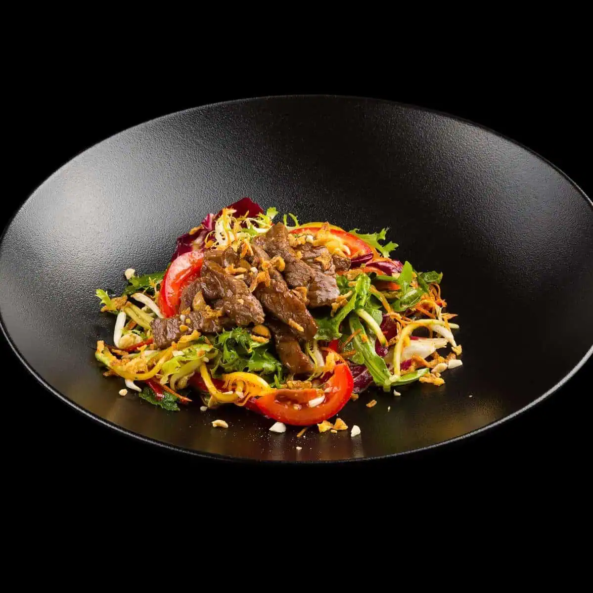 Вкусный салат с говядиной, овощами и зеленью на черной тарелке.